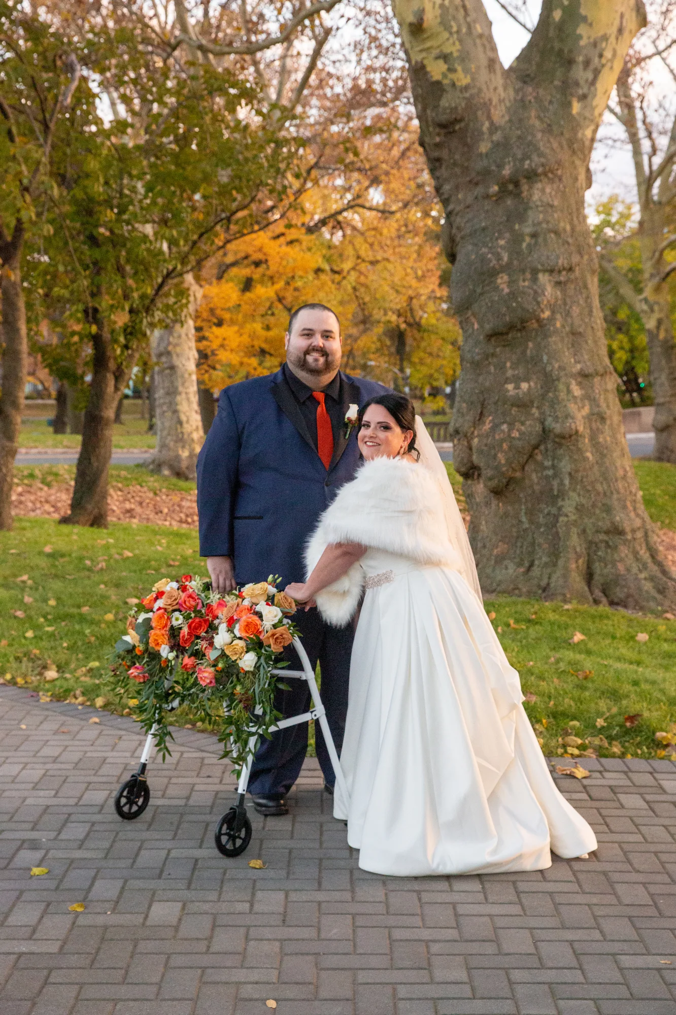 A disabled bride with a walker stands with her groom in a blue suit at a fall wedding in the Hudson Valley.