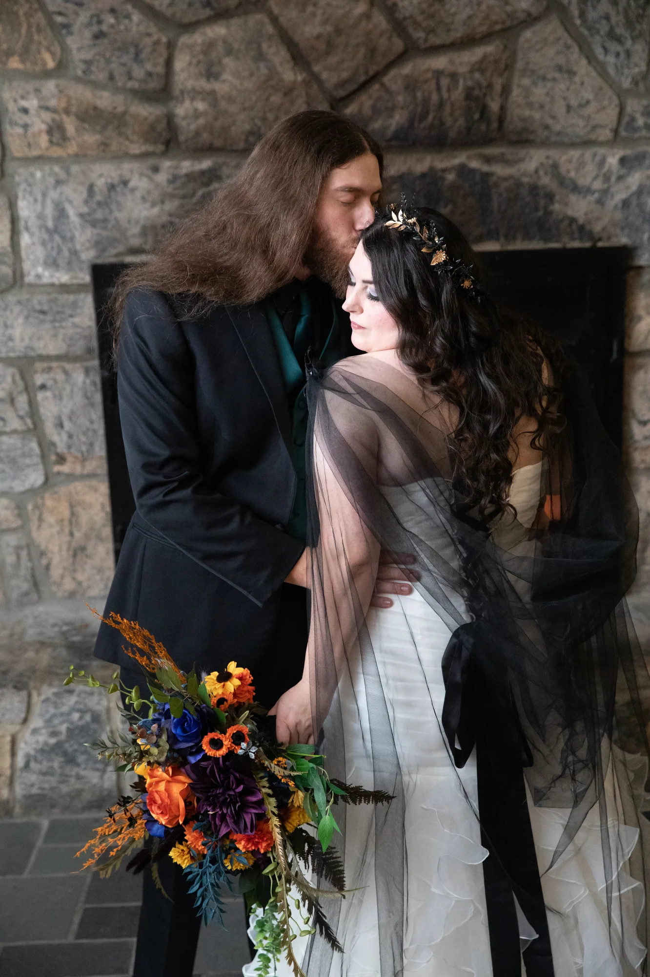 A groom with long hair kisses his bride in a white dress with a black veil at the Bear Mountain Inn.