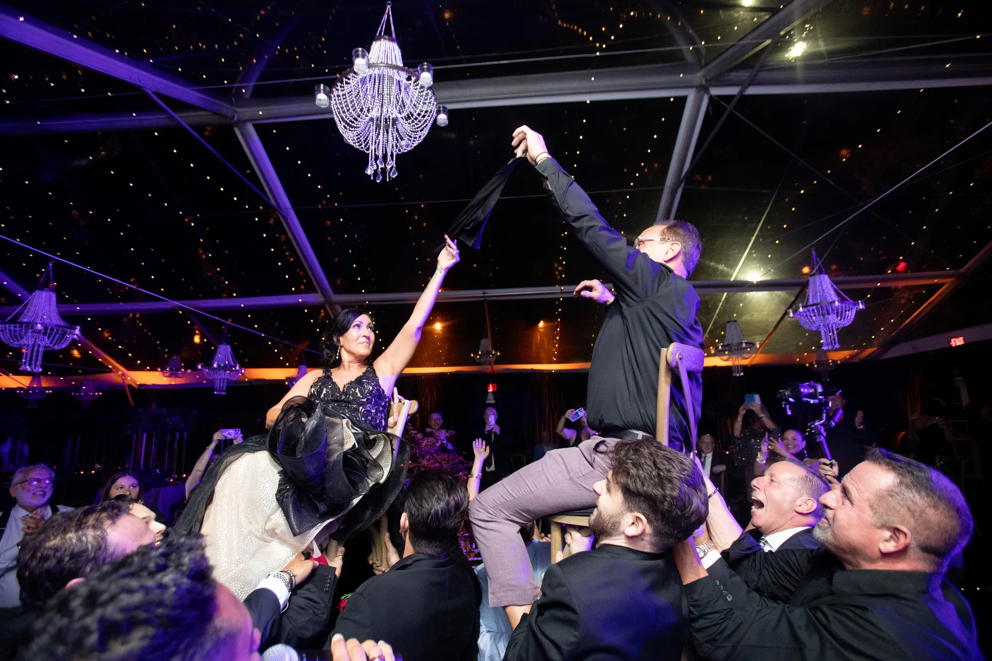 An older bride and groom are lifted in chairs during the horah at Rushmore Estate in the Hudson Valley.