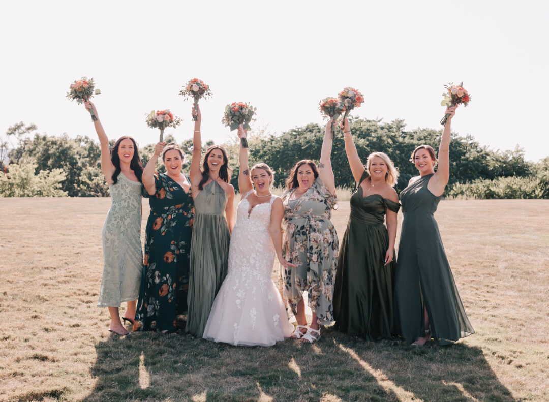 bridal party with mismatched dresses cheering and raising bouquets