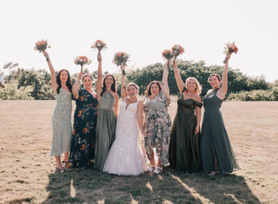 bridal party with mismatched dresses cheering and raising bouquets