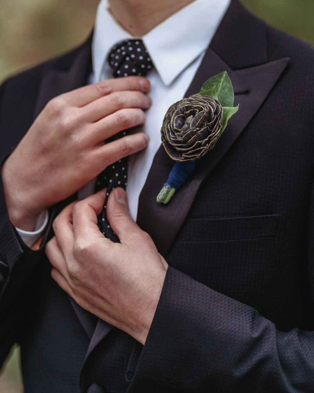 Man fixing his tie with a black rose boutonniere with gold brushed petals.