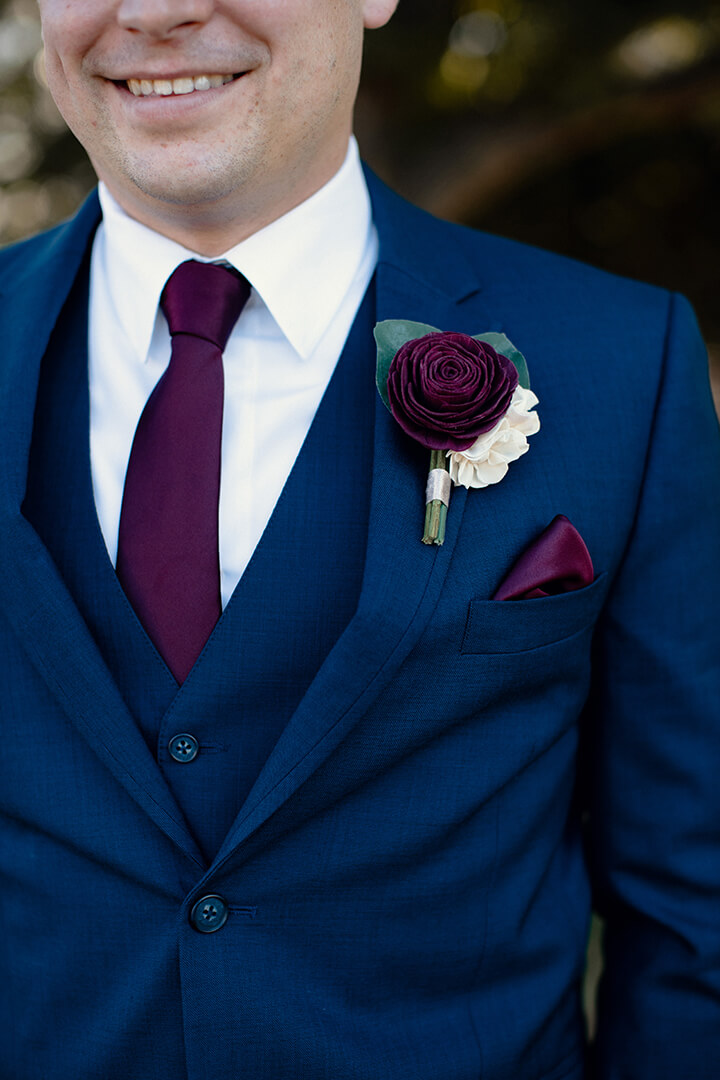 Burgundy rose boutonniere on a navy suit with navy tie and pocket square.