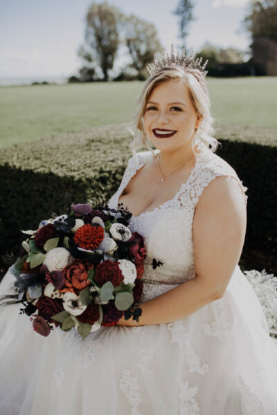 Bride wearing a crown, sitting with a large Halloween-inspired bouquet.