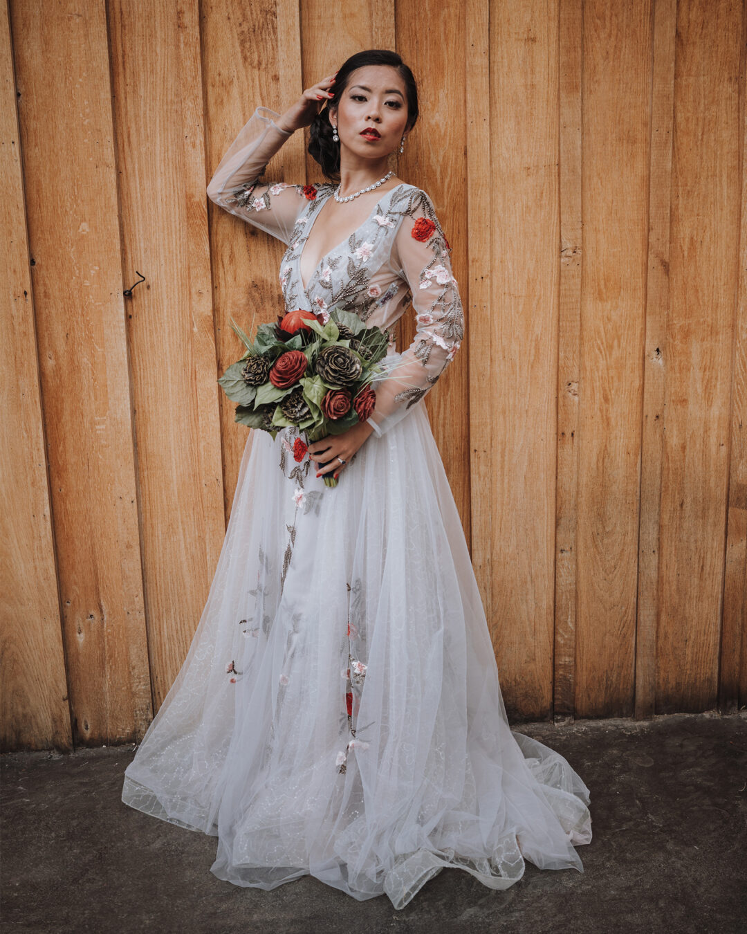Bride with floral, embroidered dress holding a bouquet of red and black wood flowers.