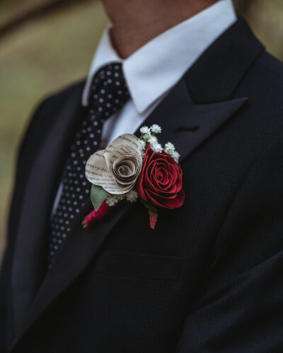 Groom with a boutonniere featuring a red wood rose and a rose made of book pages.