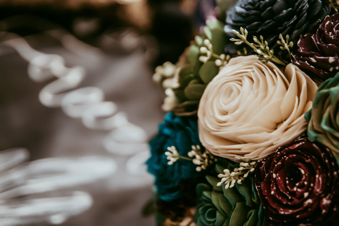 Close up photograph of ivory, teal, succlent, and purple galaxy wood flowers.