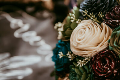 Close up photograph of ivory, teal, succlent, and purple galaxy wood flowers.