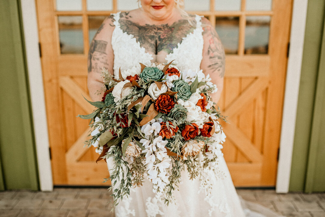 Tattooed bride with cascading bouquet of ivory, terracotta, and sage colored wood flowers.