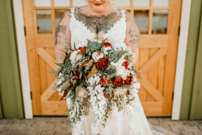 Tattooed bride with cascading bouquet of ivory, terracotta, and sage colored wood flowers.