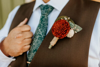 Terracotta marigold boutonniere wrapped with twine on a groom's brown vest.
