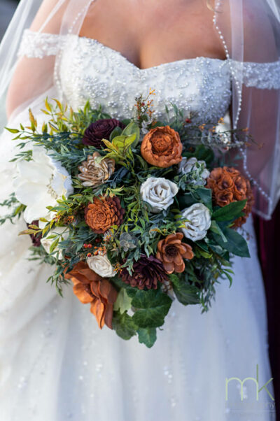 Large, cascading bouquet of faux greenery with white, burgundy, and orange wood flowers.