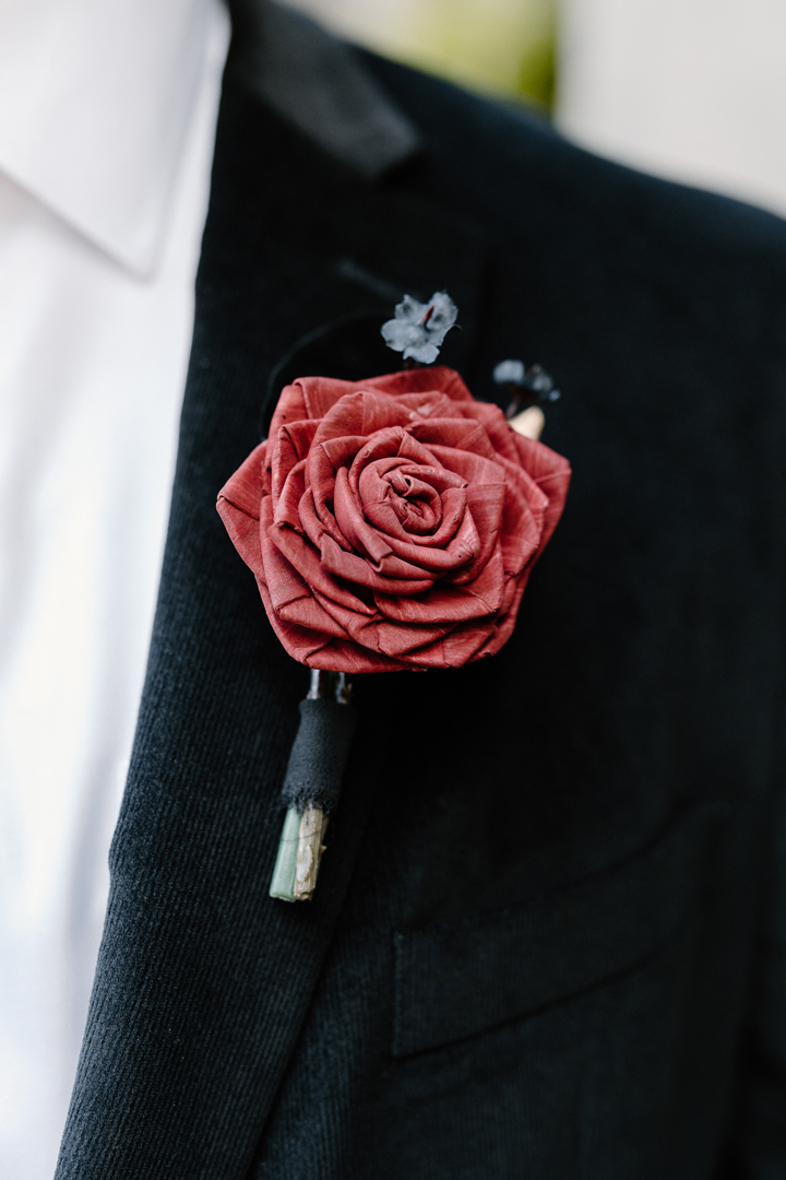 Red wood rose boutonniere with black accents and black ribbon wrapped around the stems.