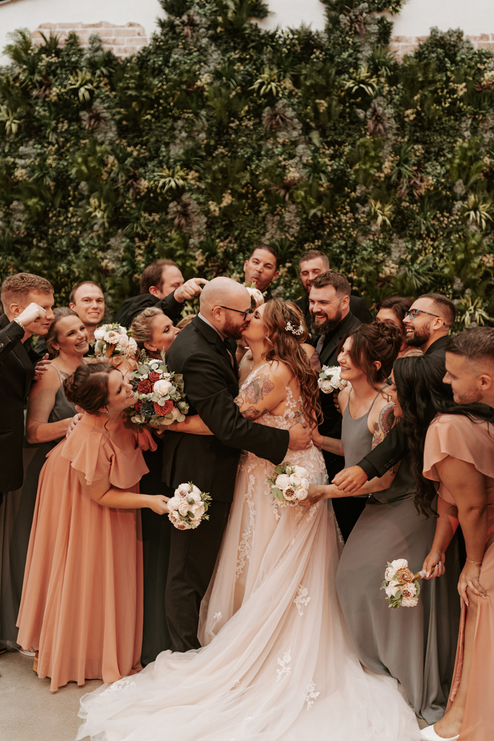 Bride and groom kissing with their wedding party crowding around them.