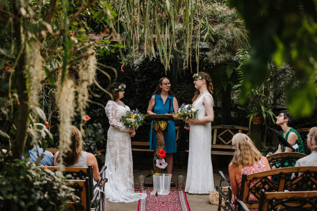 A butterfly conservatory makes for a stunning backdrop for this elopement. A natural frame of tropical plants surrounds the couple and their guests.