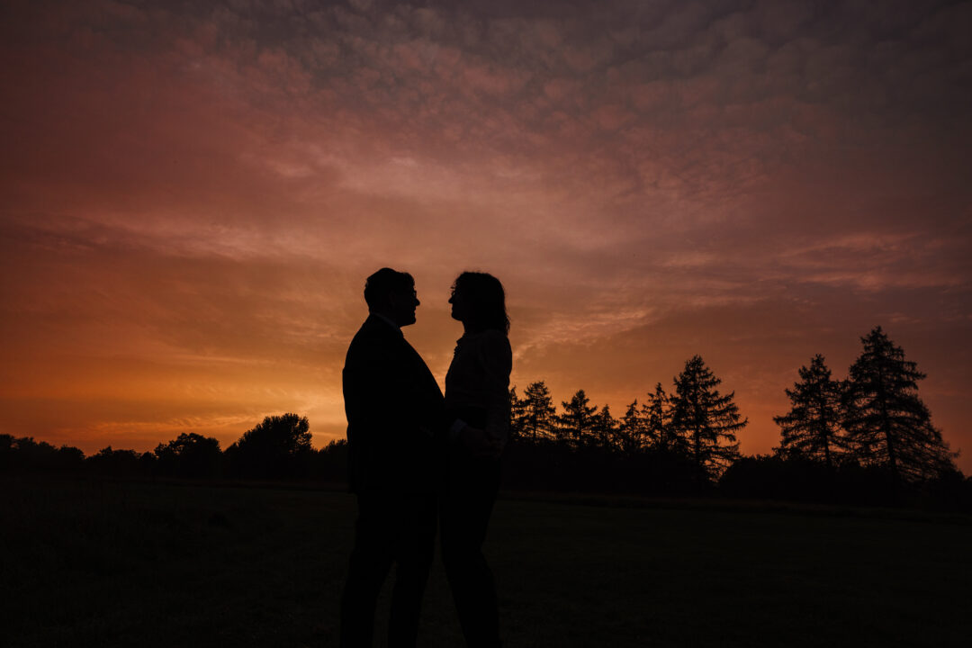 Two people stand face to face and create a silhouette against the golden sunset sky behind them