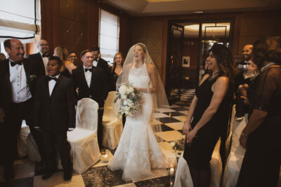 The bride, in a mermaid white dress, with her cascading peony bouquet walks towards the ceremony