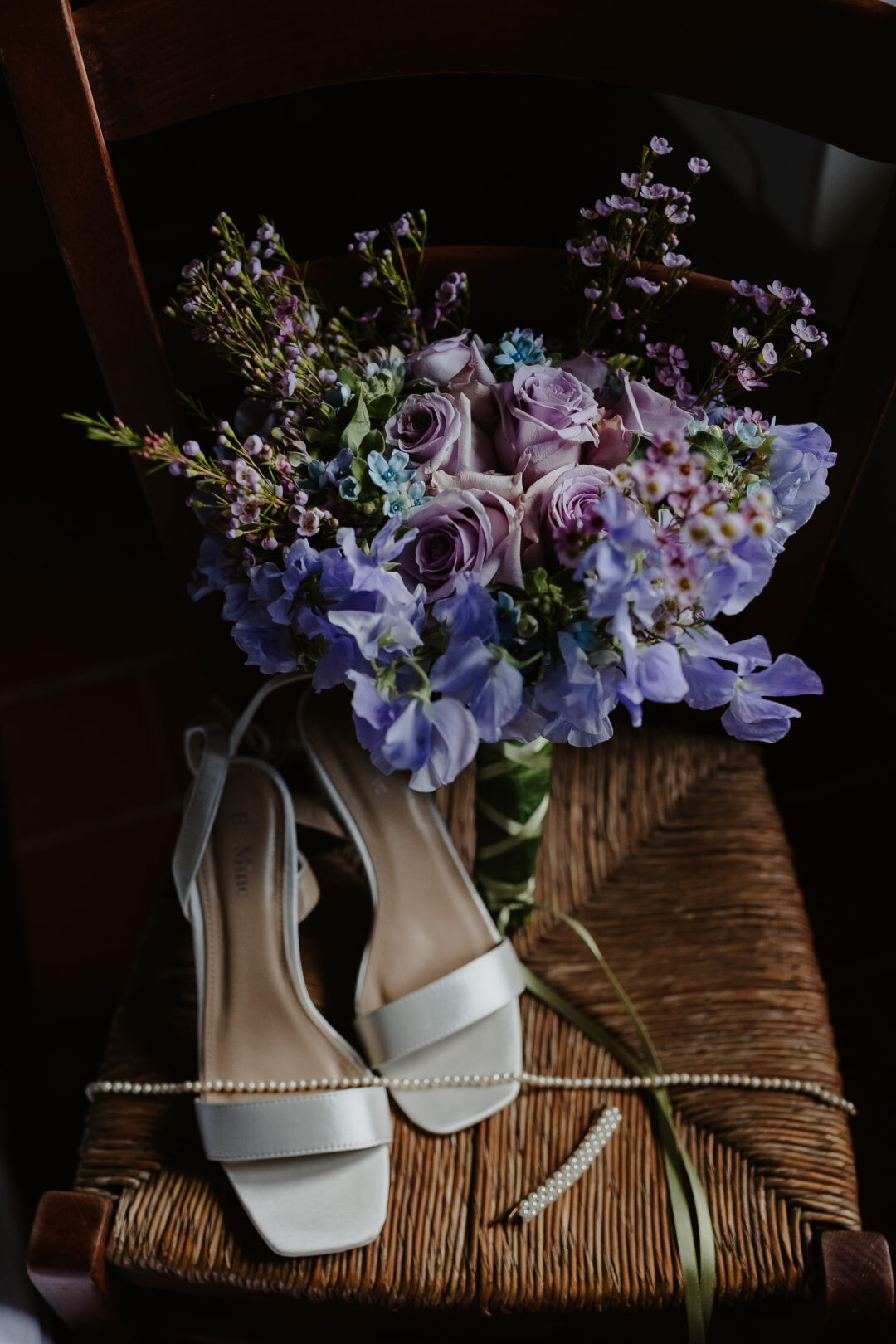 Purple and lavender hued bouquet, with delicate roses and sweet pea, above the bridal shoes