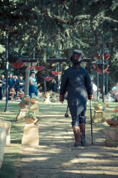 Black and burgundy steampunk groom surrounded by umbrellas hanged open and upside down, walking towards the ceremony, right in front of the guests.
