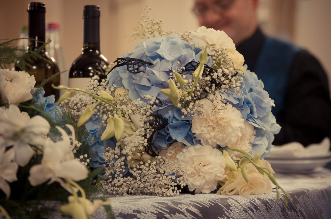 A bouquet with white roses, orchids and carnations, with blue hydrangeas and black macramé lace dragon wings