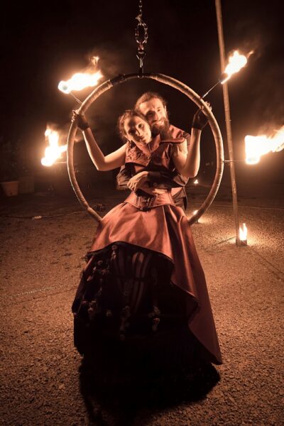 The bride sits on a circular support with four fire torches above, the groom stands behind her for the photo.