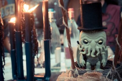 A little Chthulhu funko pop with a tall black hat stands besides lighted black candles.