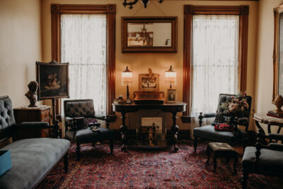 Blue velvet couches in a room decorated with antique furniture, books, lamps, and lace curtains