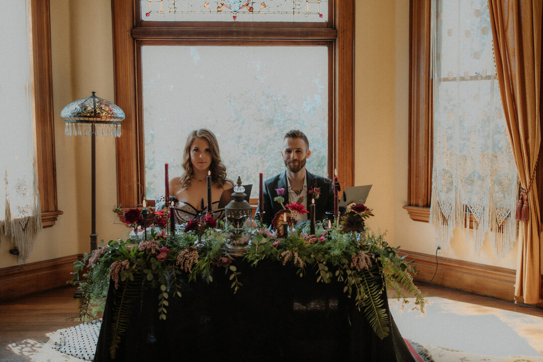 A bride and groom sit at an opulently decorated sweetheart table in the Fireside room at the Victorian Belle Mansion in North Portland. Photo by Megan Gallagher