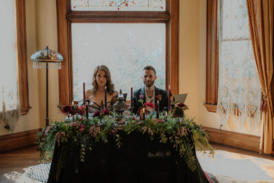 A bride and groom sit at an opulently decorated sweetheart table in the Fireside room at the Victorian Belle Mansion in North Portland. Photo by Megan Gallagher