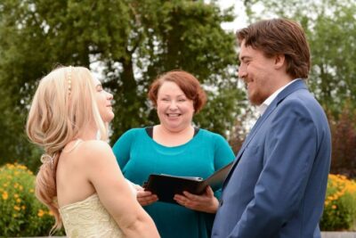 Officiant stands with a couple holding hands during an outdoor garden wedding ceremony.