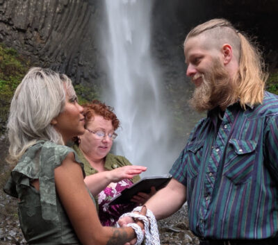 edding officiant performs a handfasting ceremony for a couple in front of a waterfall in Oregon.