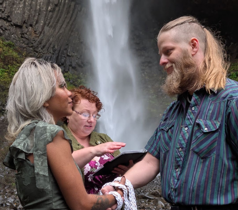 edding officiant performs a handfasting ceremony for a couple in front of a waterfall in Oregon.