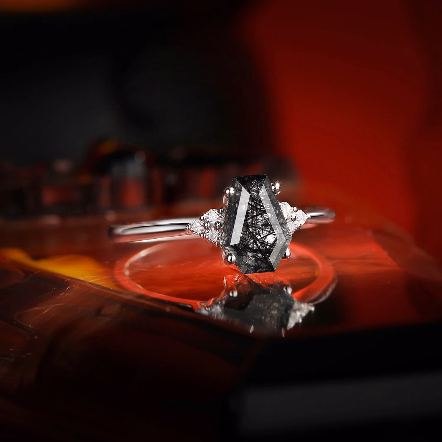Alternative engagement ring featuring a coffin-cut black rutilated quartz center stone with small white diamond accent clusters set in a delicate silver band, photographed against a dramatic red background by StarlandUS