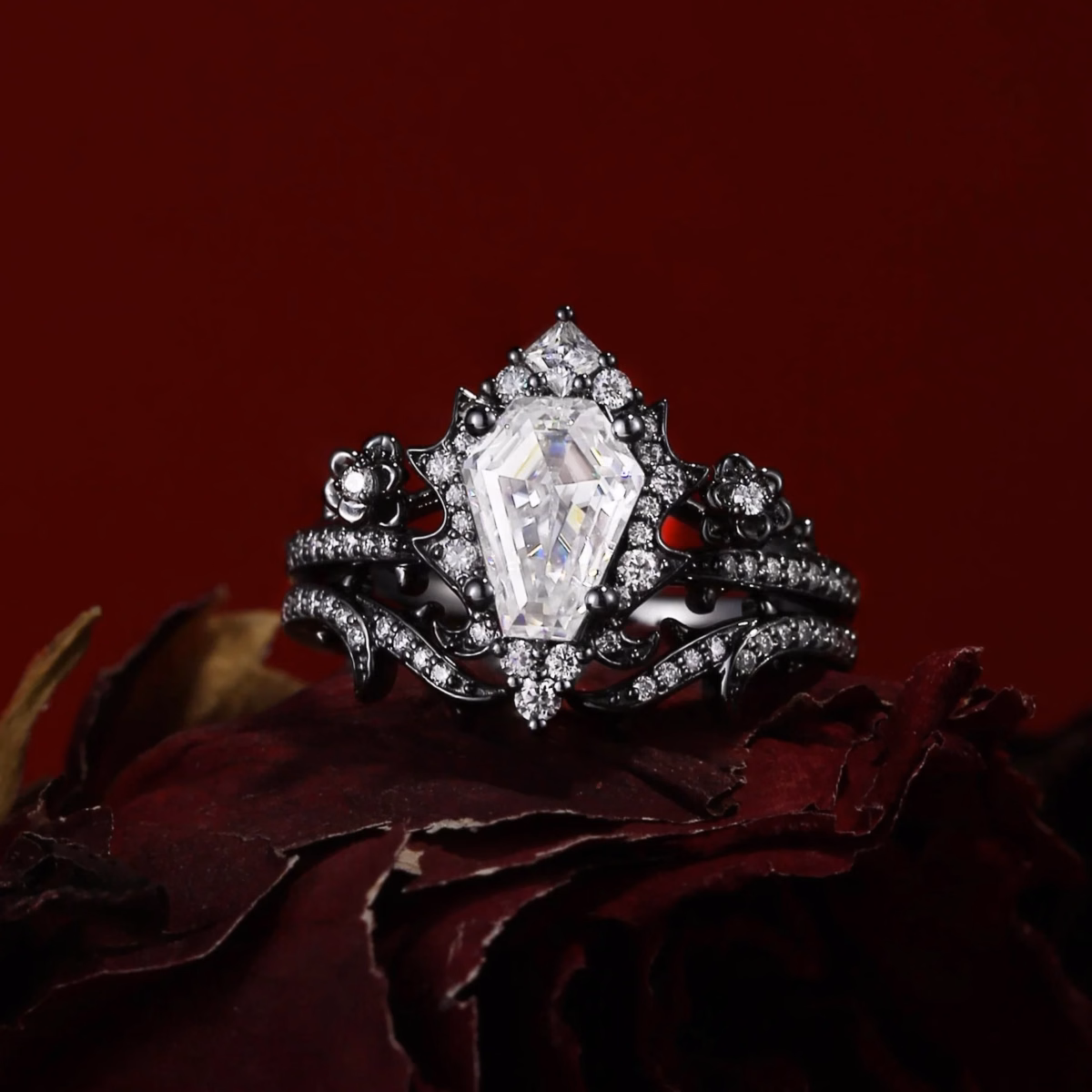 Gothic-style engagement ring set featuring a coffin-cut white moissanite center stone in a black rhodium setting with floral details and pavé accent stones, displayed on a deep red dried rose, by StarlandUS