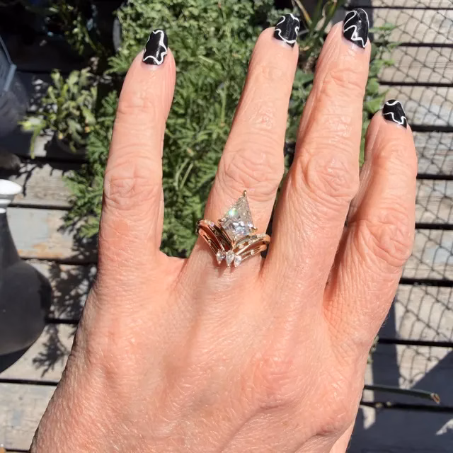 Close-up of a hand with black-and-white nail art displaying a stacked ring set featuring a large princess-cut diamond engagement ring and gold wedding band from StarlandUS alternative engagement rings collection