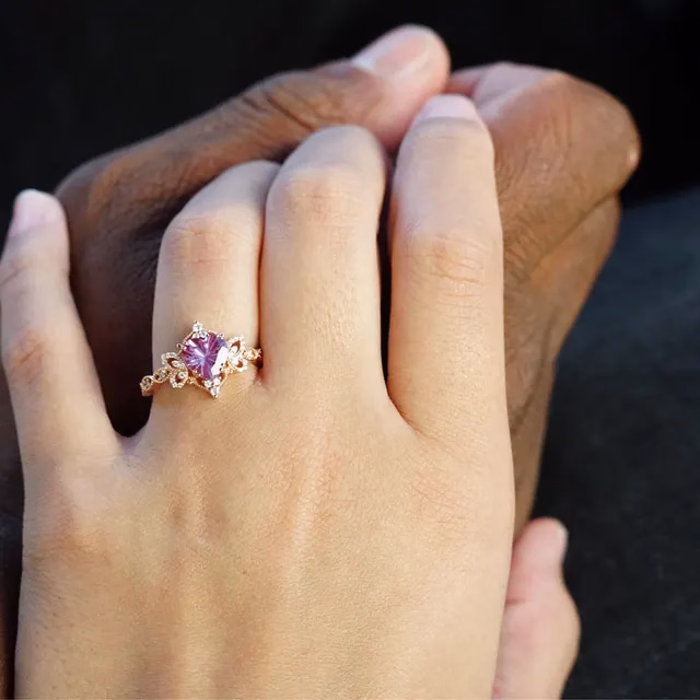 A decorative rose gold ring with a pink cushion-cut gemstone and floral diamond detailing worn on a ring finger, two hands holding together, alternative engagement ring by StarlandUS